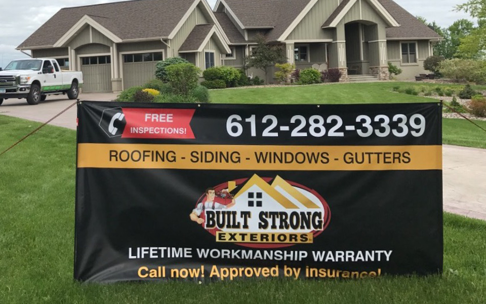 A remodeled home with new roofing and siding provided by Built Strong Exteriors with their banner in the front yard.
